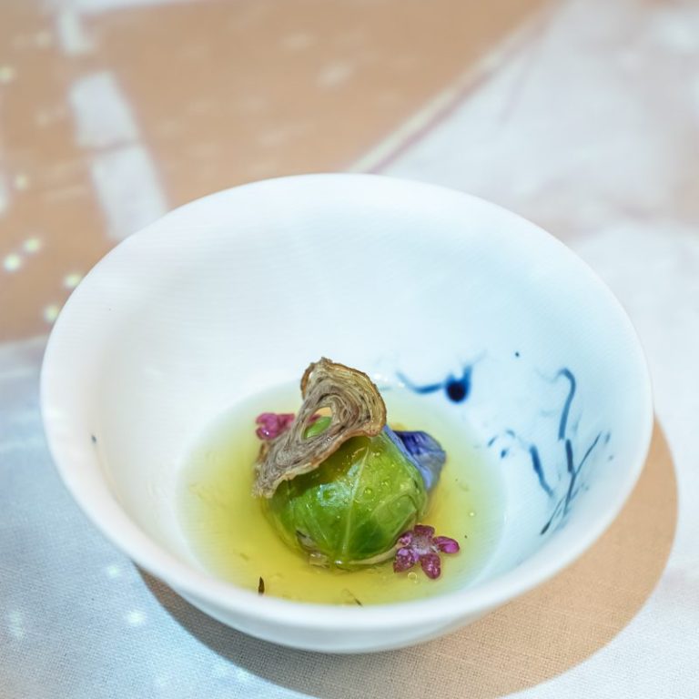 Bouillon Homard Andouille choux de Bruxelles Un plat gastronomique avec un choux farci, des fleurs comestibles et une garniture créative.